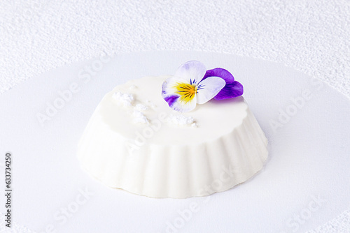 Panna cotta decorated with edible violet flower on white background © twomeerkats