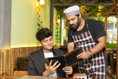 Young indian boy ordering food to waiter at restaurant