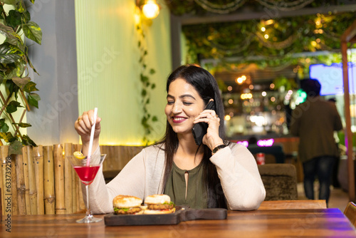 Indian woman talking on mobile phone while eating food at restaurant.