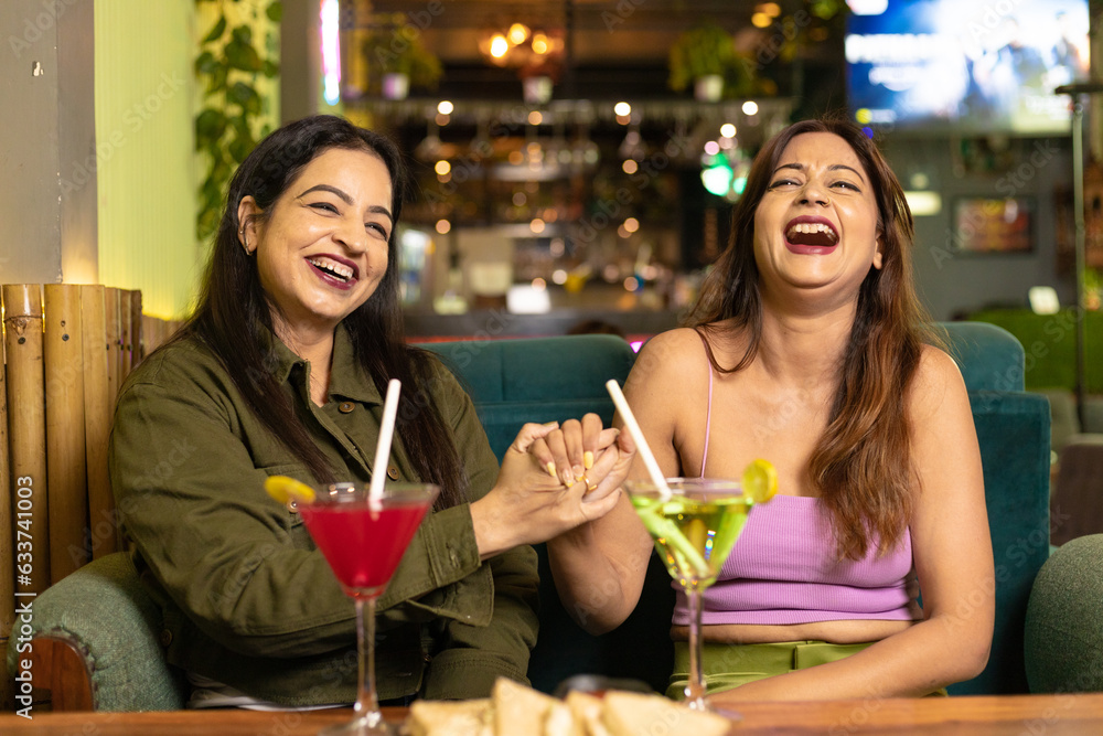 Two indian female friends discussing, laughing and enjoying party together at restaurant.