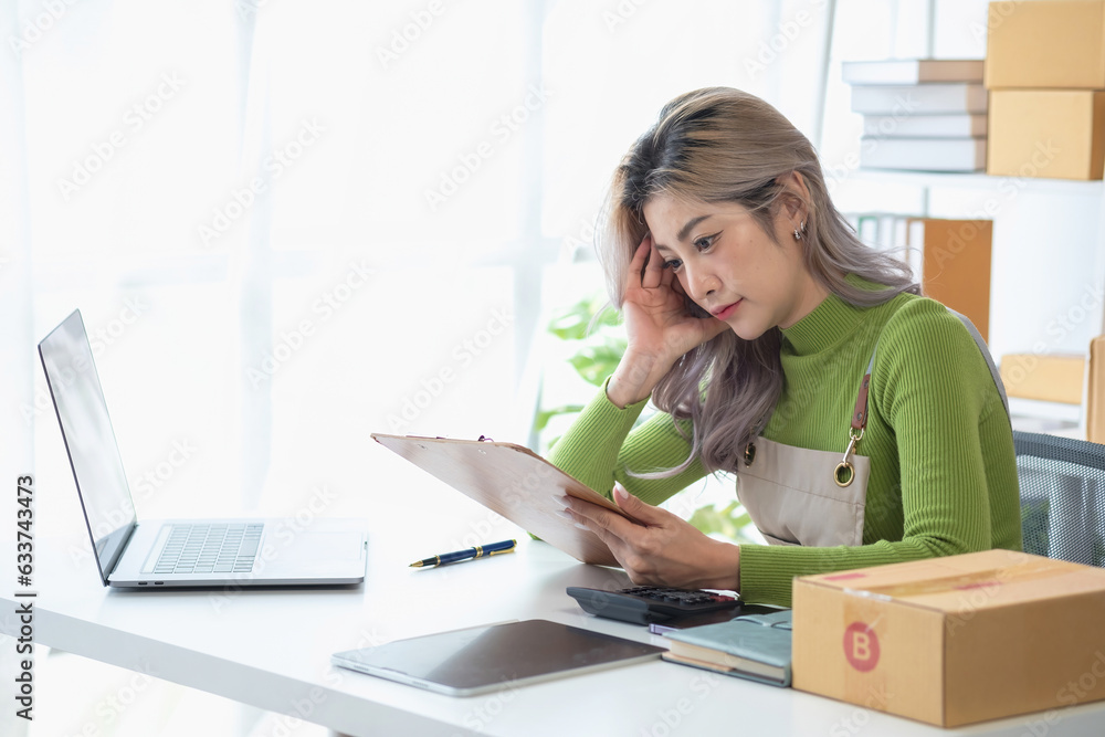Asian woman with a beautiful face, and white skin, online shopping businessman, worried about low sales orders, causing stress in SME business, online shopping business concept. Asian woman with a beautiful face, and white skin, online shopping businessman, worried about low sales orders, causing stress in SME business, online shopping business concept.
