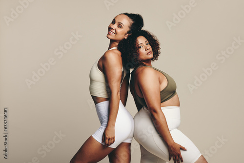 Female athletes show off their toned bodies as they stand back to back in a studio