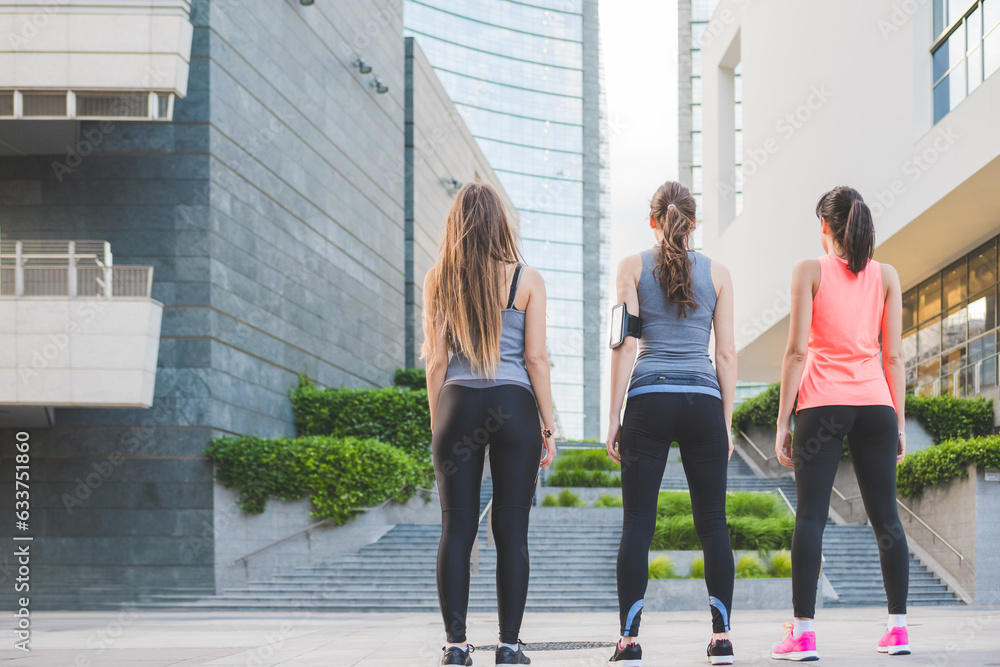 Back view of determined three young millennial sportive women outdoor in the city