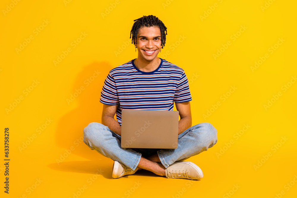 Full size portrait of cheerful nice person sit floor crossed legs use netbook networking isolated on yellow color background Full size portrait of cheerful nice person sit floor crossed legs use netbook networking isolated on yellow color background