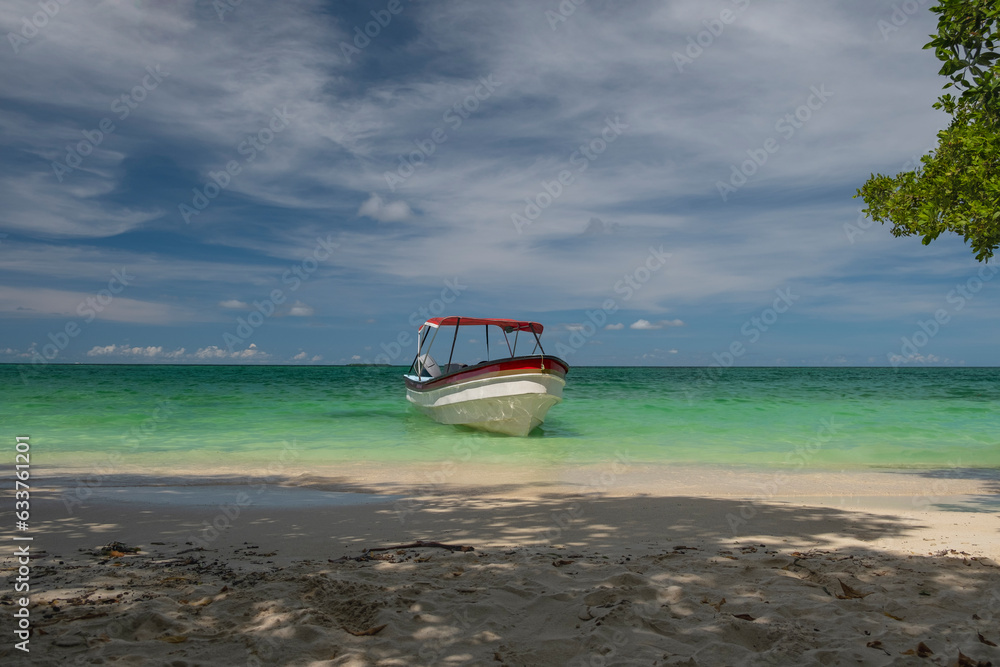 Tour boat moored by the shore at hidden secluded sandy beach, clear blue sky and see thru turquoise ocean water in the background. Isla Grande, Colombia.