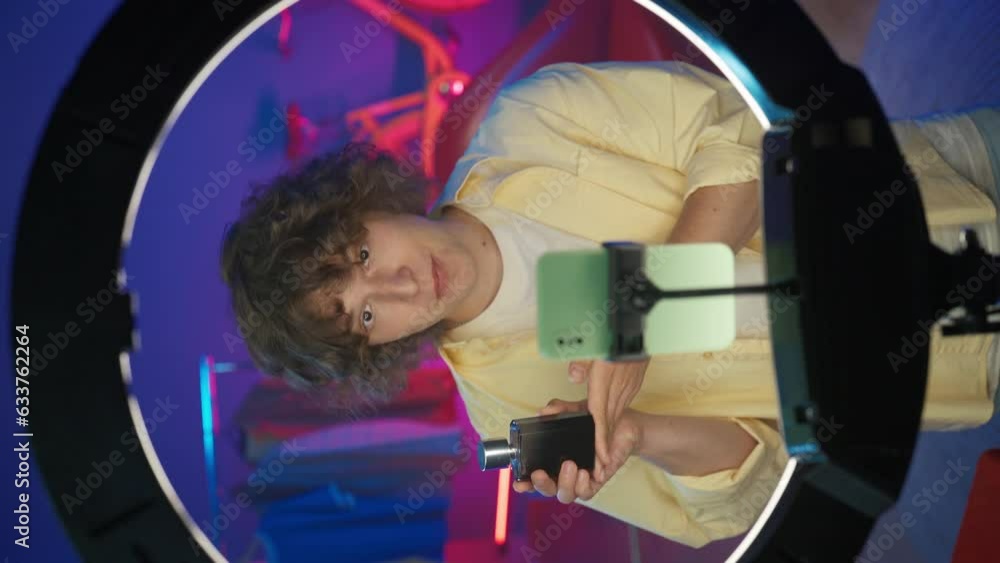 Young man vlogger in casual clothing advertises a perfume in front of his smartphone at home studio. Vertical video Young man vlogger in casual clothing advertises a perfume in front of his smartphone at home studio. Vertical video