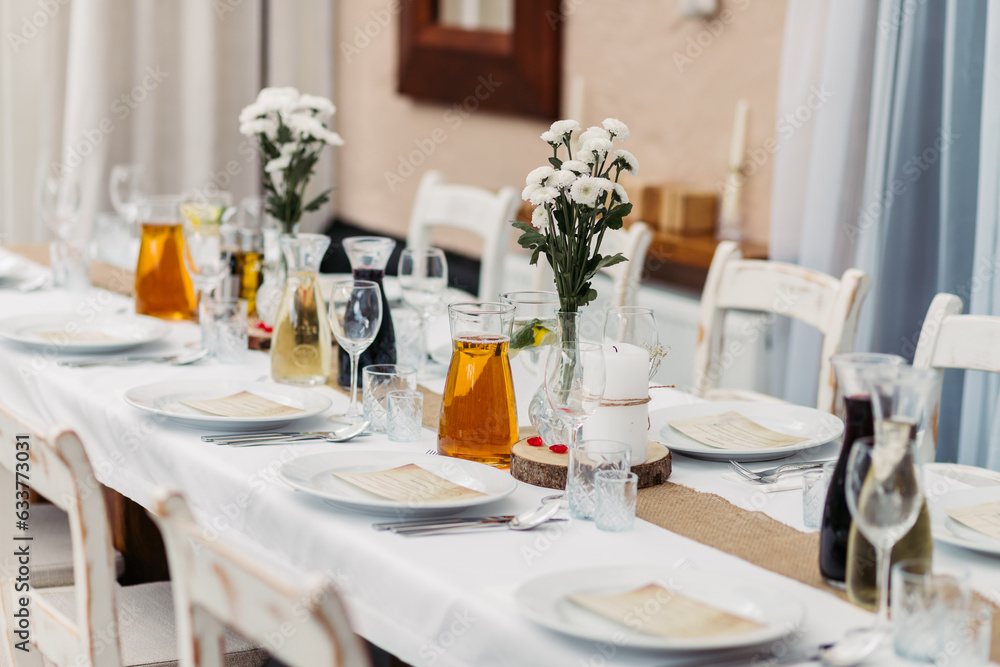 Empty table set for a wedding. Table setting in white colors with flowers. Transparent vases with wild flowers on the table. Plates with menu cards. Glasses on the table and alcoholic drinks.