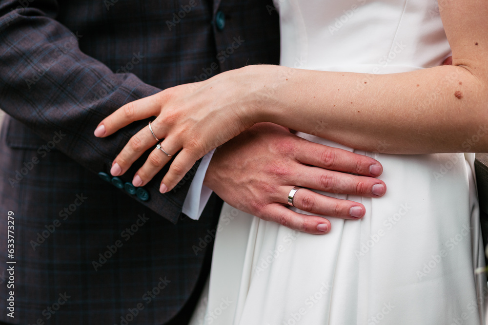 A girl in a white dress and a groom in a classic suit. The man holds the bride by the waist. Hands of the bride and groom with wedding rings. wedding details. Outdoor wedding photo session. A girl in a white dress and a groom in a classic suit. The man holds the bride by the waist. Hands of the bride and groom with wedding rings. wedding details. Outdoor wedding photo session.