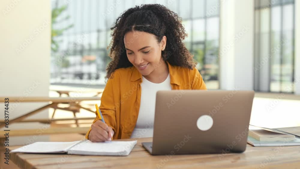 Trendy lovely positive brazilian or hispanic curly young woman, university student, sitting outdoors near campus, with laptop and notebook, preparing for exam, smile. Successful female freelancer Trendy lovely positive brazilian or hispanic curly young woman, university student, sitting outdoors near campus, with laptop and notebook, preparing for exam, smile. Successful female freelancer