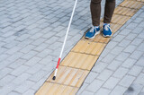 Close-up of a woman's legs with a cane near a tactile tile.