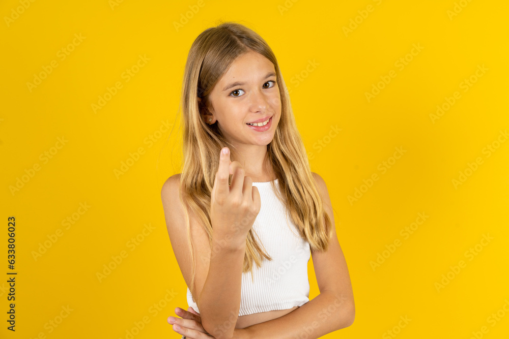 blonde kid girl wearing white T-shirt over yellow studio background Beckoning come here gesture with hand inviting welcoming happy and smiling blonde kid girl wearing white T-shirt over yellow studio background Beckoning come here gesture with hand inviting welcoming happy and smiling