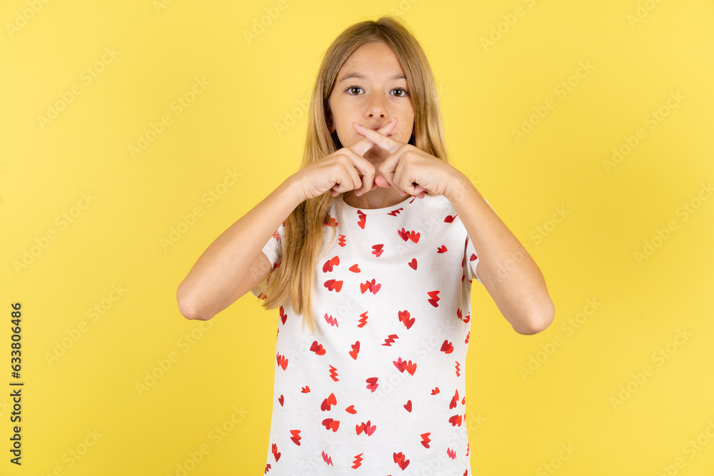 blonde kid girl wearing polka dot shirt over yellow studio background Has rejection angry expression crossing fingers doing negative sign. blonde kid girl wearing polka dot shirt over yellow studio background Has rejection angry expression crossing fingers doing negative sign.