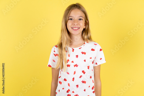 blonde kid girl wearing polka dot shirt over yellow studio background with a happy and cool smile on face. Lucky person.