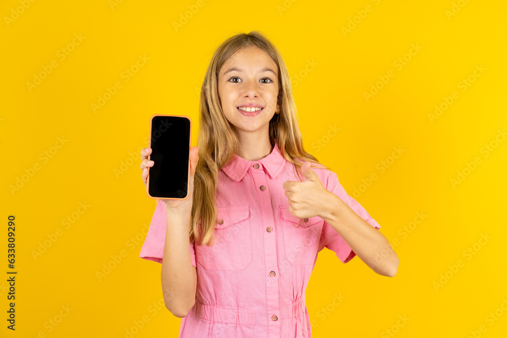 young beautiful blonde kid girl over yellow studio background Show blank screen smartphone, thumb up recommend new app young beautiful blonde kid girl over yellow studio background Show blank screen smartphone, thumb up recommend new app