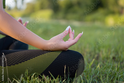 Meditation in nature for a healthy lifestyle: a girl performs complex asanas while sitting on a green lawn close-up.