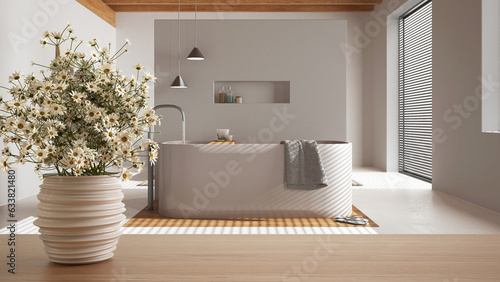 Wooden table top or shelf with pottery vase with daisies, wild flowers, over modern white bathroom with bathtub and resin floor, minimalist interior design concept photo