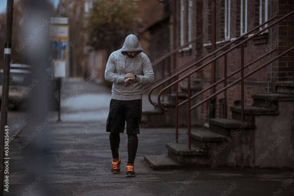 Young man using a smart phone before jogging and exercising on a sidewalk in the city