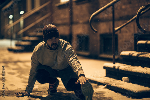 Fototapeta Naklejka Na Ścianę i Meble -  Young man stretching before jogging and exercising in the snow in the city during winter