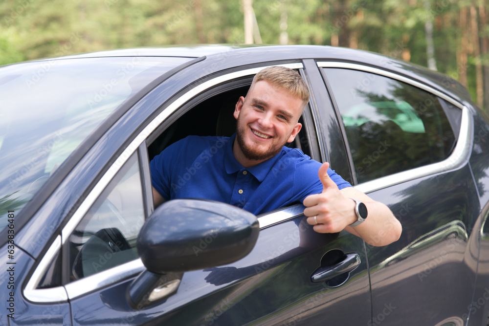 Young happy man with his new car show thumb up, like gesture with finger. Satisfied customer, driver. 