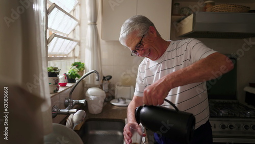 Mature man serving coffee with thermos bottle into glass by kitchen sink. Authentic domestic scene of retired older person starting the day ritual morning