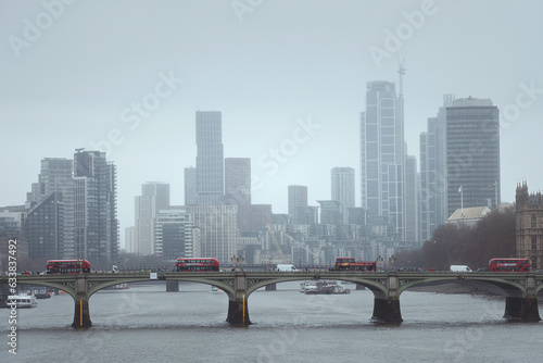 London's iconic Westminister Bridge with red buses crossing the River Thames, surrounded by a stunning view of the city with skyscrapers in the morning. MARCH 20, 2023. United Kingdom photo