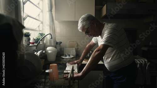 Struggling Senior man leaning on kitchen counter suffering from difficultires and preoccupation lifting head to window feeling angst