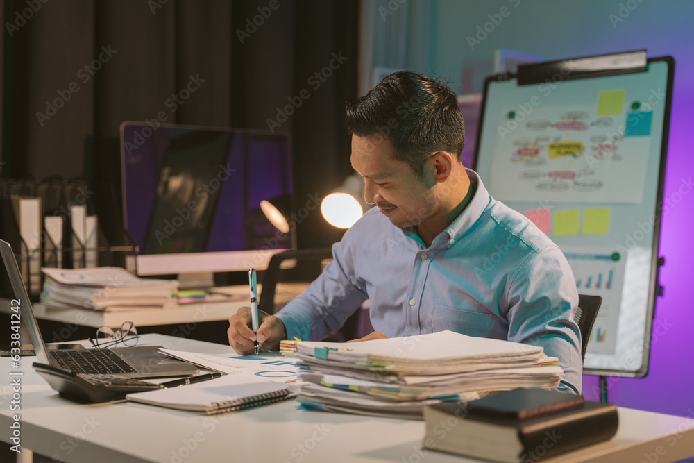 Naklejka premium Young Asian businessman talking on the phone late night hustle ambitious Working overtime talking on the phone in the organization