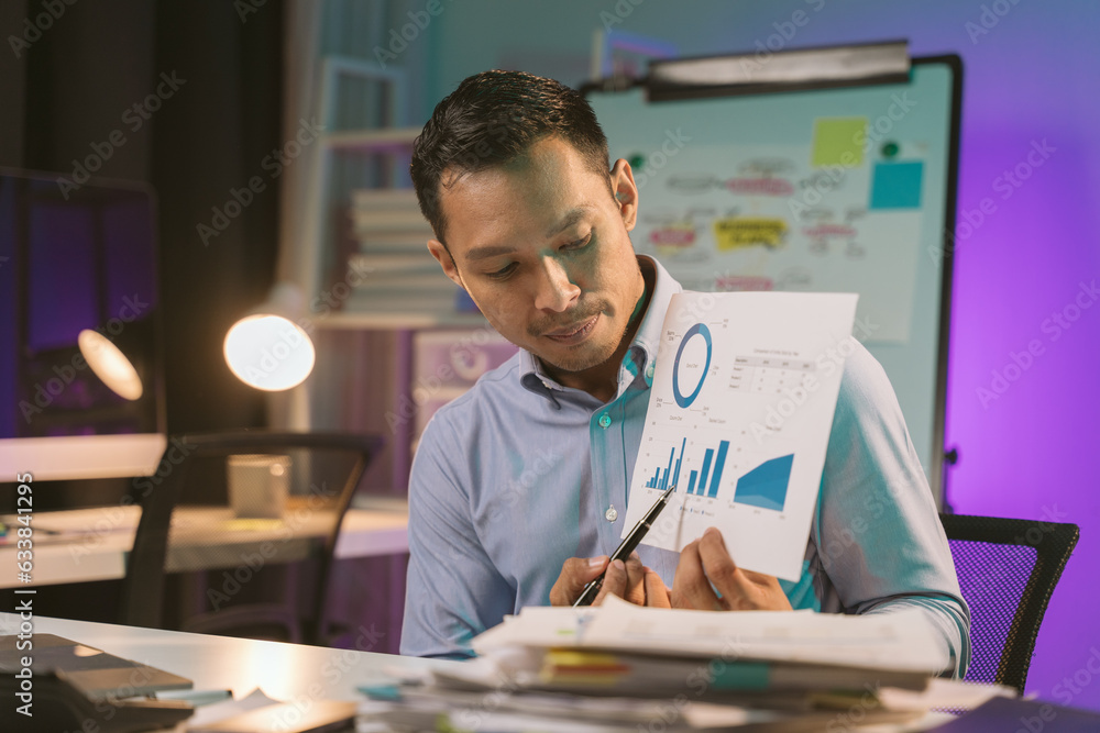 Fototapeta premium Young Asian businessman talking on the phone late night hustle ambitious Working overtime talking on the phone in the organization