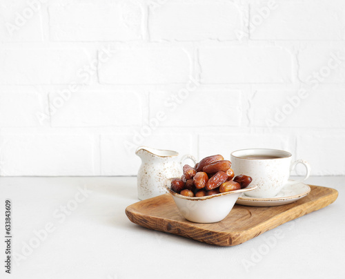 Dried dates in a bowl, tea in a wooden tray on white background. Healthy breakfast. Natural oriental sweets. Copy space. photo