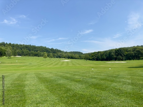 A view of a hill with a green golf course on a sunny day. Golf course with flags and sand bunkers. Green grass and trees with white sand trap.