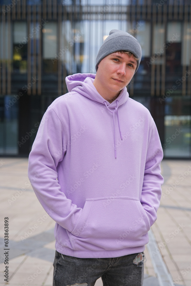 Portrait of young happy man or teenager in hoodie and hat looking at camera outdoors