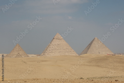 The three pyramids of Egypt side by side in the middle of desert sand with the sky in the background