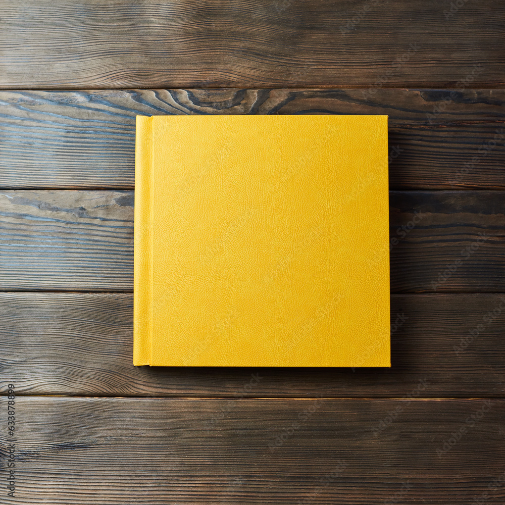 Yellow hardcover photobook isolated on a wooden background with copy space. Top view, flat lay. Blank closed book mockup for placing custom text or images. Stylish wedding or family photo book. Yellow hardcover photobook isolated on a wooden background with copy space. Top view, flat lay. Blank closed book mockup for placing custom text or images. Stylish wedding or family photo book.