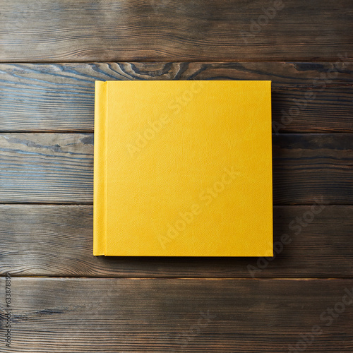 Yellow hardcover photobook isolated on a wooden background with copy space. Top view, flat lay. Blank closed book mockup for placing custom text or images. Stylish wedding or family photo book.