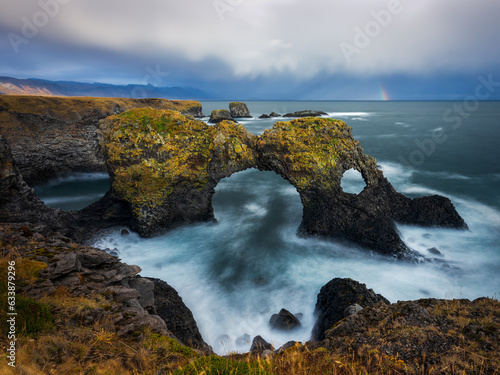 Scenic panorama of Gatklettur sea arch in Arnarstapi, Snaefelsness, Iceland. Cloudy day with a rainbow.