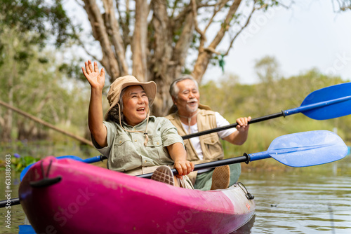 Asian senior couple kayaking together in the lake at mangrove forest on summer vacation. Retired elderly people man and woman have fun outdoor lifestyle travel nature and rowing a boat in the river.