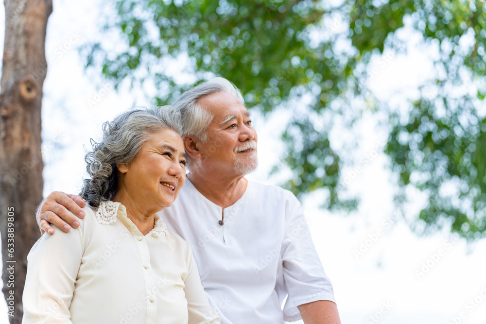 Happy Asian family senior couple with gray hair resting together at tropical beach at summer sunset. Retired elderly people enjoy romantic outdoor lifestyle travel nature ocean on holiday vacation.
