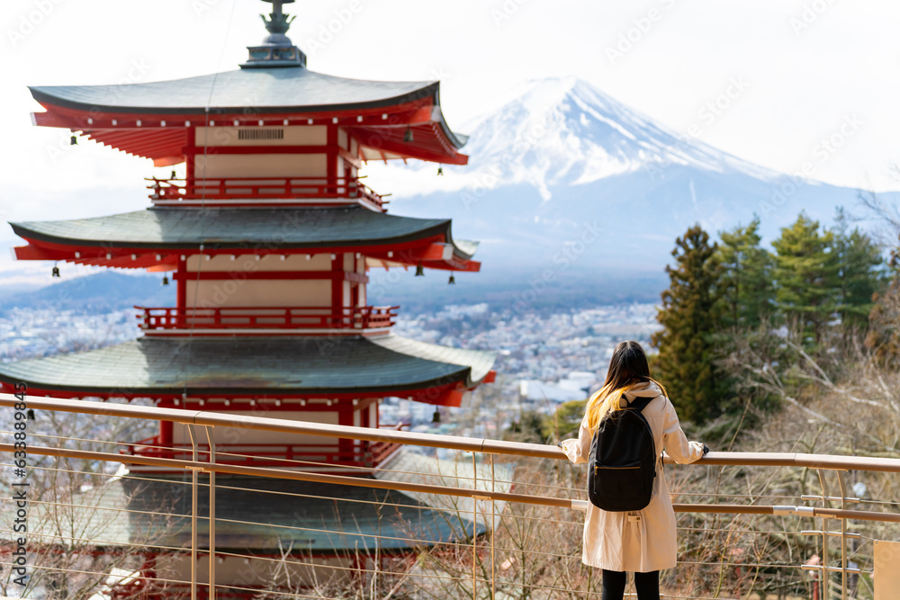 Happy Asian woman enjoy outdoor lifestyle travel at red Chureito Pagoda with Mt Fuji covered background in winter holiday vacation. People travel Japan landmark famous place and season change concept. - obrazy, fototapety, plakaty 
