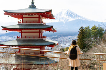 Happy Asian woman enjoy outdoor lifestyle travel at red Chureito Pagoda with Mt Fuji covered background in winter holiday vacation. People travel Japan landmark famous place and season change concept.