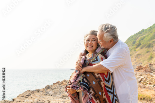 Asian family senior couple hugging each other on coastline beach at sunset. Retirement elderly people enjoy outdoor lifestyle travel ocean on summer vacation. Old person mental health care concept.