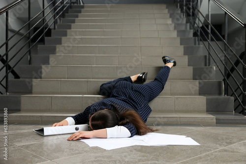 Fotografie Unconscious woman with scattered folder and papers lying on floor after falling