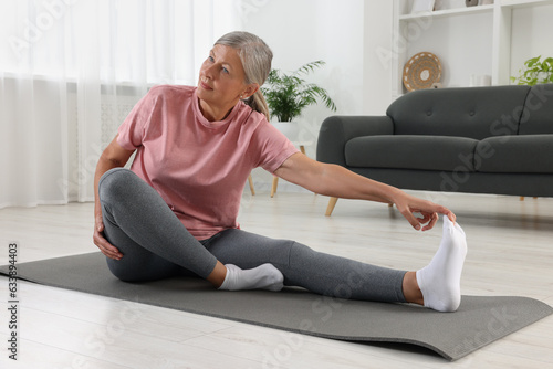 Senior woman in sportswear stretching on fitness mat at home