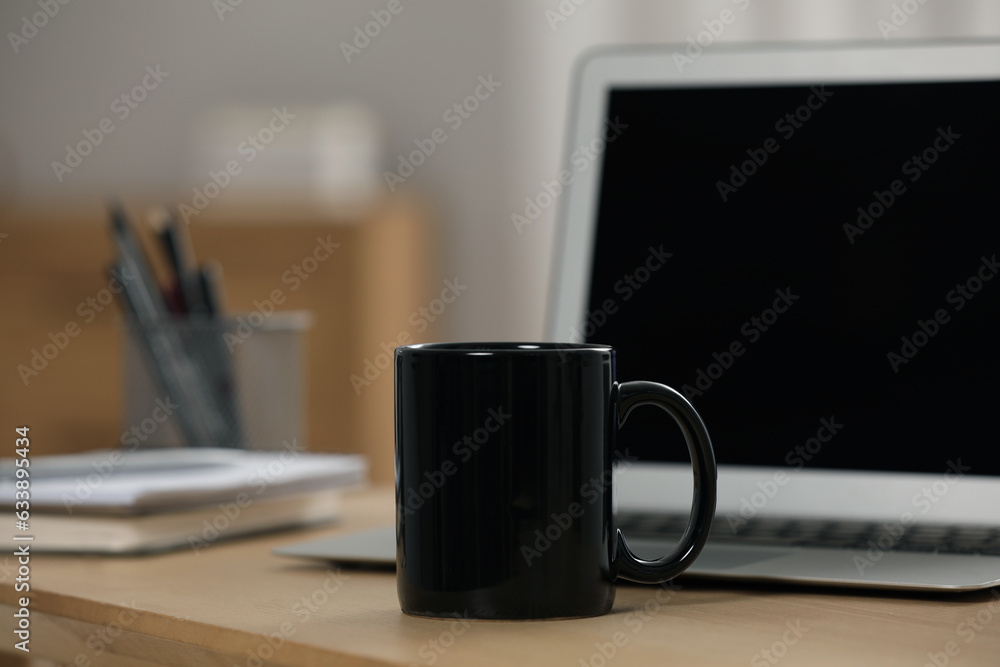 Black ceramic mug and laptop on wooden table at workplace Black ceramic mug and laptop on wooden table at workplace