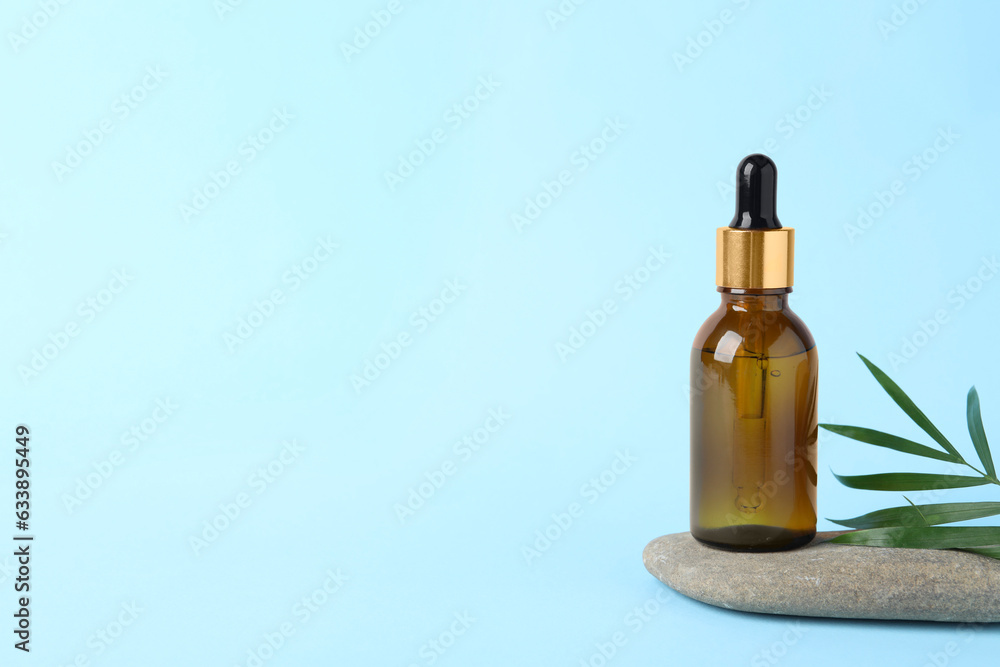 Bottle with cosmetic oil, stone and green leaf on light blue background, space for text