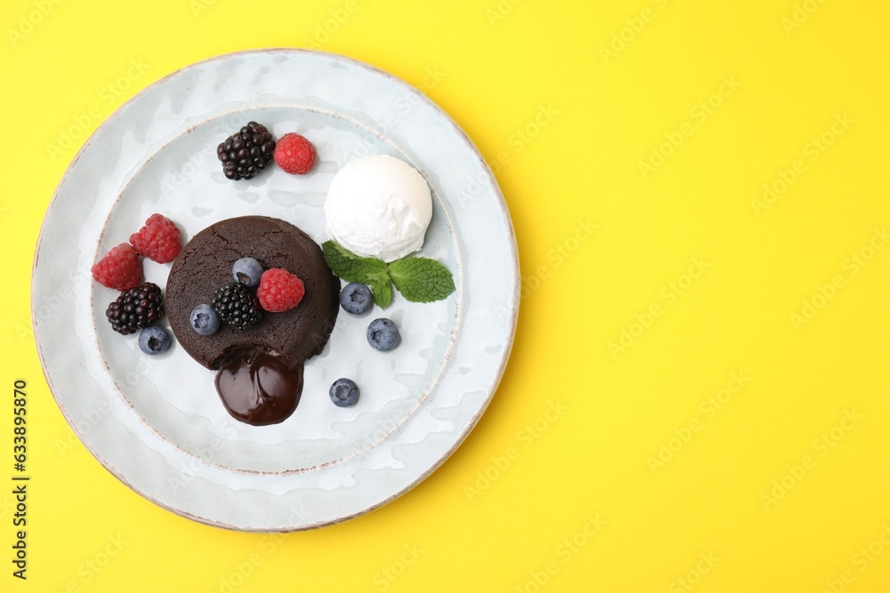 Fototapeta premium Delicious chocolate fondant served with fresh berries and ice cream on yellow background, top view. Space for text