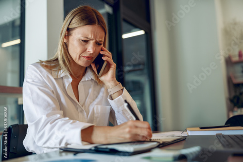Принти на полотні Worried woman entrepreneur making notes and talking by phone with client while s