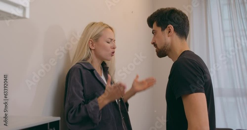 young couple quarreling at home and yelling at each other. guy hit the wall. Caucasian man attacks an attractive young fair-haired woman. Grabs her by the shoulders, Screaming The victim of violence