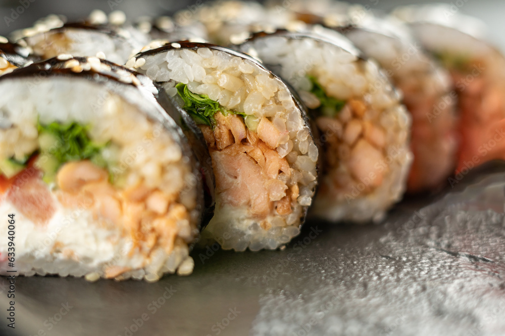 sushi roll with salmon, avocado, cream cheese, cucumber, rice on black background sushi roll with salmon, avocado, cream cheese, cucumber, rice on black background