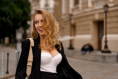 Beautiful smiling woman in elegant black suit  posing outdoor in old european city.  Blond wavy hairs, perfet skin. © Svetlana Sokolova