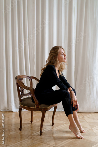 Indoor studio photo of elegant blond woman sitting on the chair. Casual fashion look. Elegance, seductive mood.